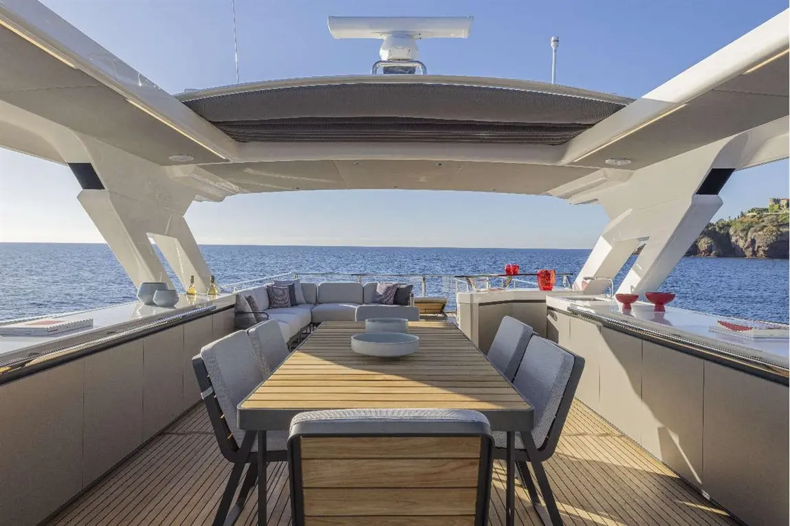 Luxury yacht deck featuring a dining table, comfortable seating, and an ocean view under clear skies.